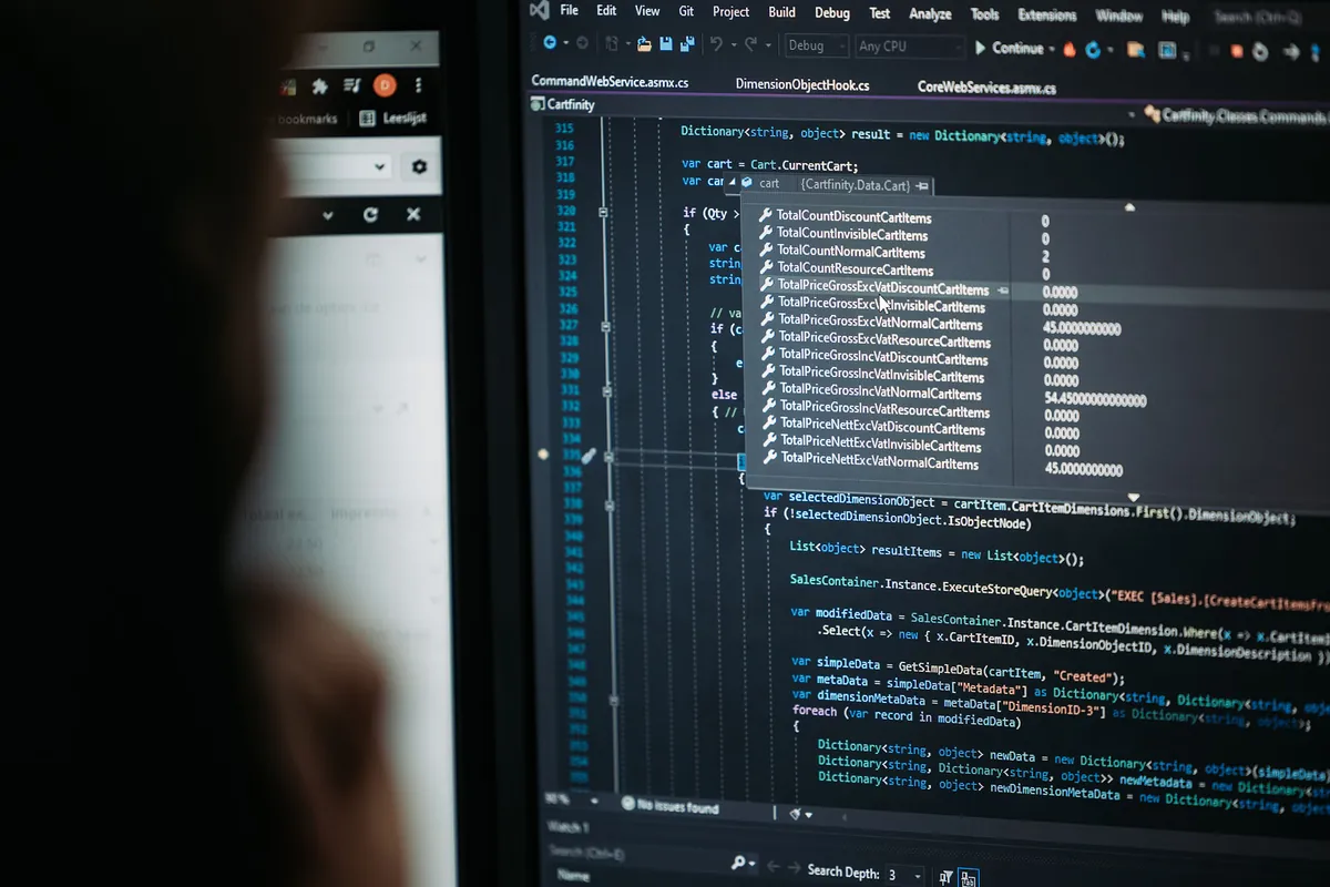 Programmeercode op een scherm bij Infodatek Group, met een collega op de voorgrond.