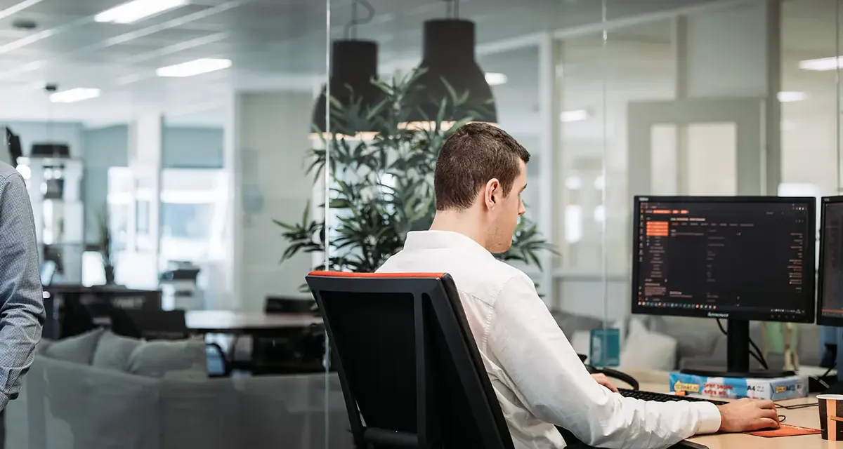 Een engineer van Infodatek Group achter zijn scherm, met glazen wanden en planten op de achtergrond.