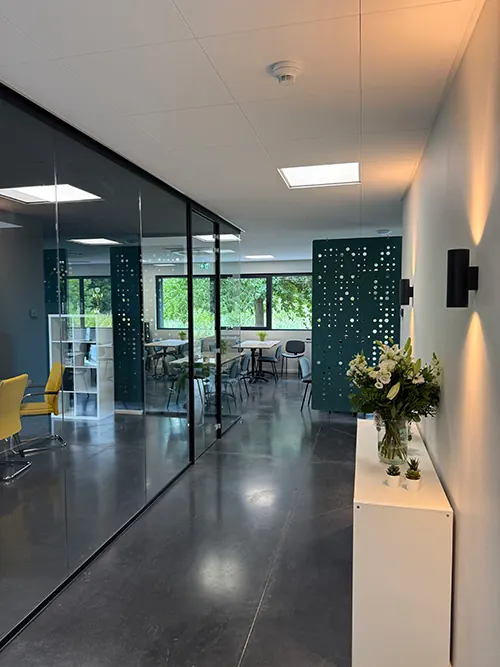 Een lichte gang in het kantoor van Infodatek Group, met glazen wanden en bloemen.