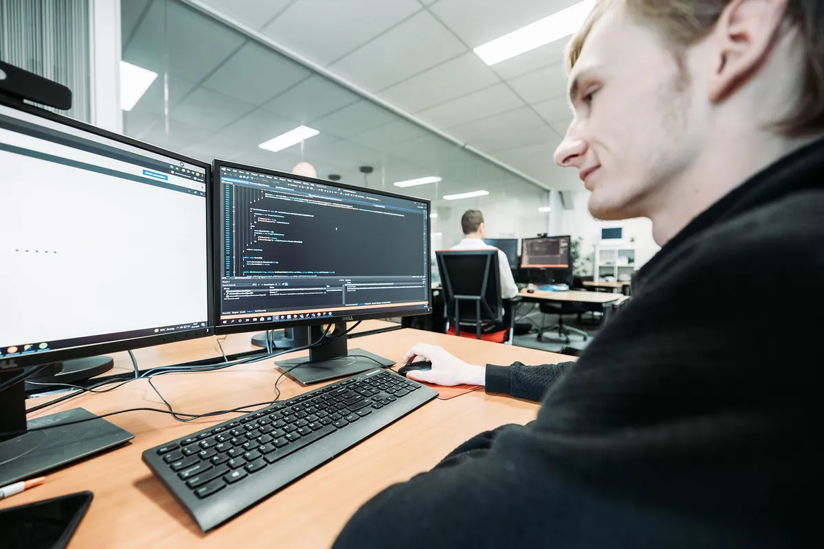 Een software-engineer van Infodatek Group aan het werk achter twee schermen.