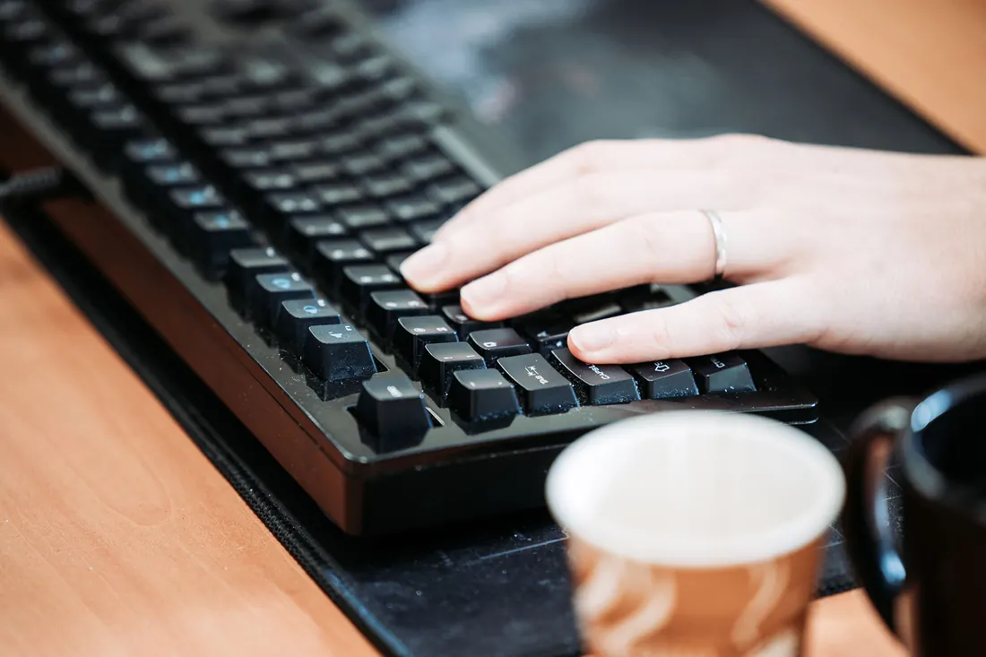 Een hand op het toetsenbord met een kop koffie ernaast.
