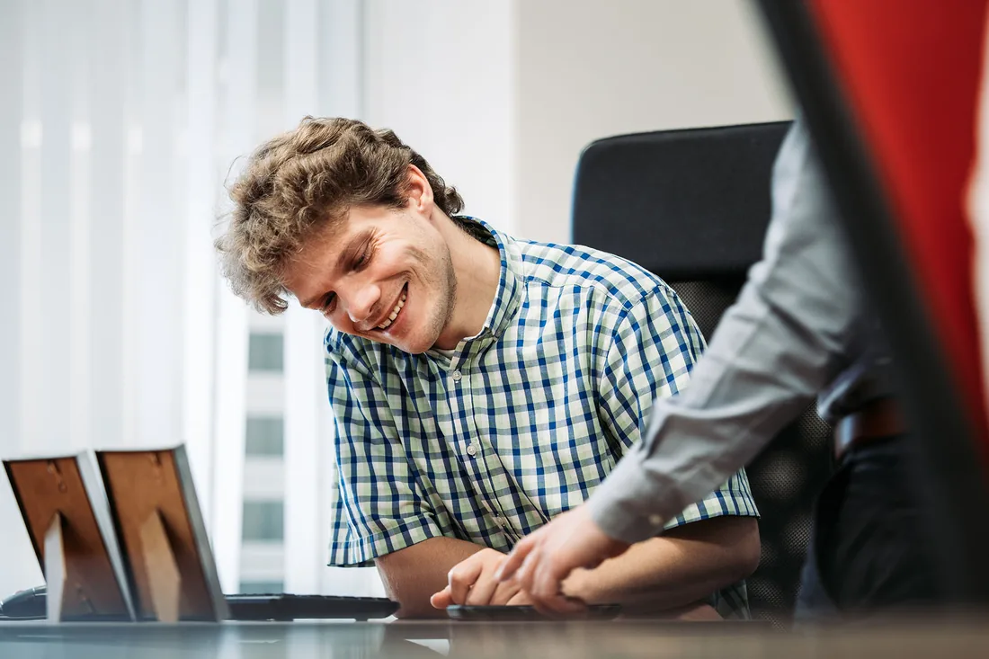 Een collega van Infodatek Group lacht achter zijn laptop terwijl een collega naast hem meekijkt en iets aanwijst.