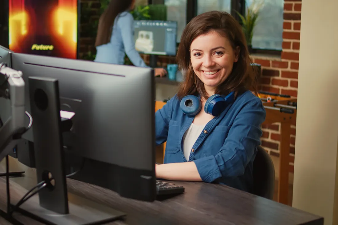 Een lachende IT-medewerker achter haar computer, met een koptelefoon om de nek.